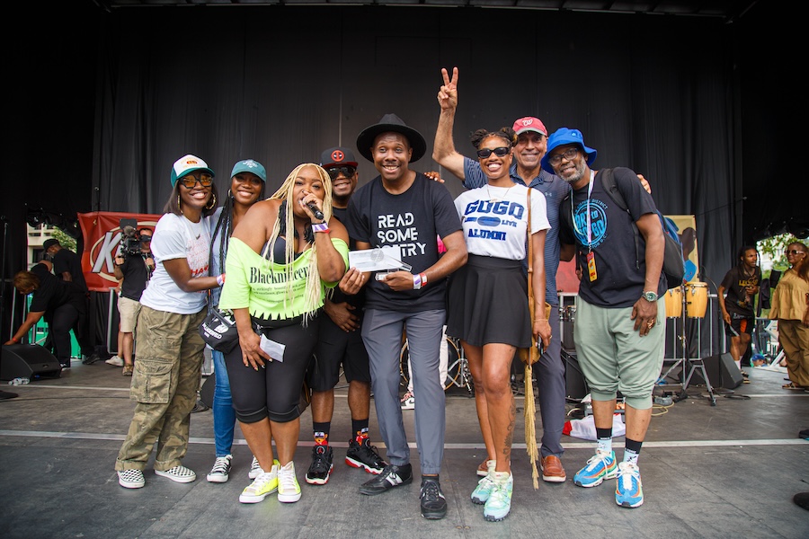 A lively group of eight people posing happily on stage at the Giant National BBQ Battle, with some holding microphones and one flashing a peace sign.