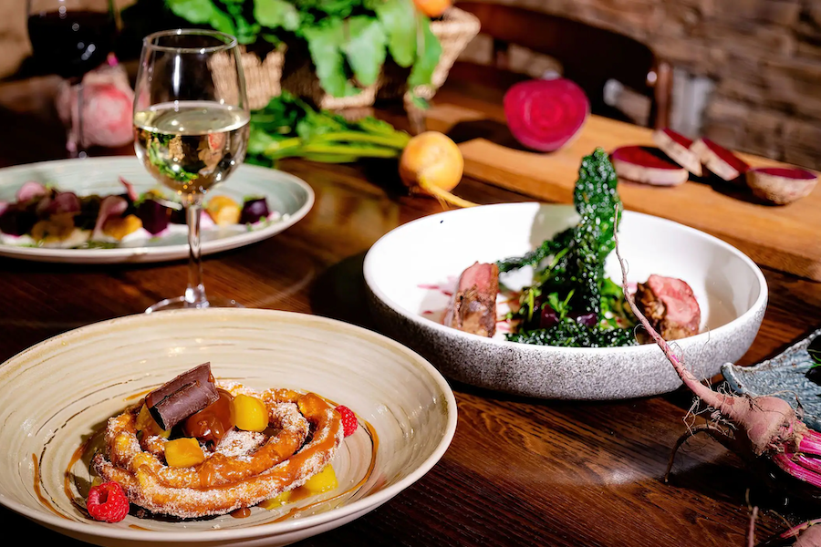 a table with plates of curated, modern food with farm produce in the background 