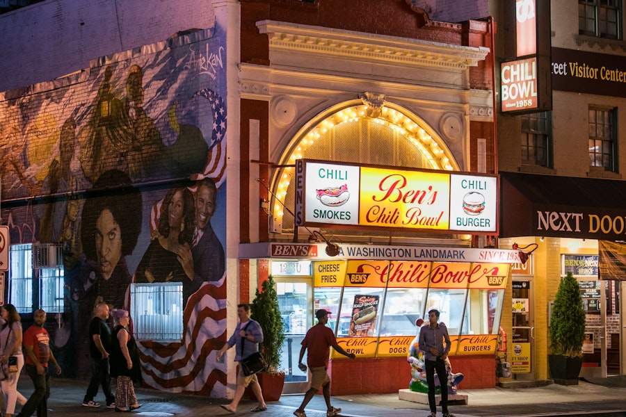 The iconic Ben's Chili Bowl, lit up at night with a mural of notable figures painted on the adjacent wall.