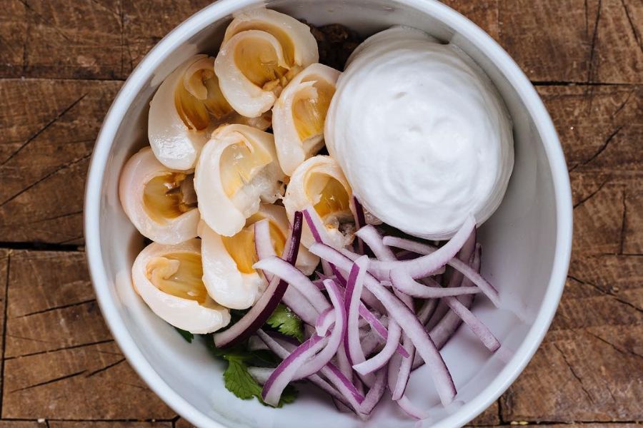 a close-up of the pork & lychee salad from Rose's Luxury with lychees, red onions and coconut cream in a white bowl