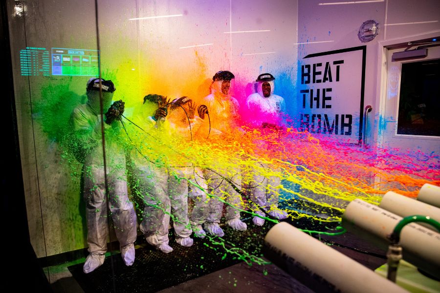 Players in white suits get blasted with colorful paint as they attempt to 'Beat the Bomb' in this high-energy, immersive experience.