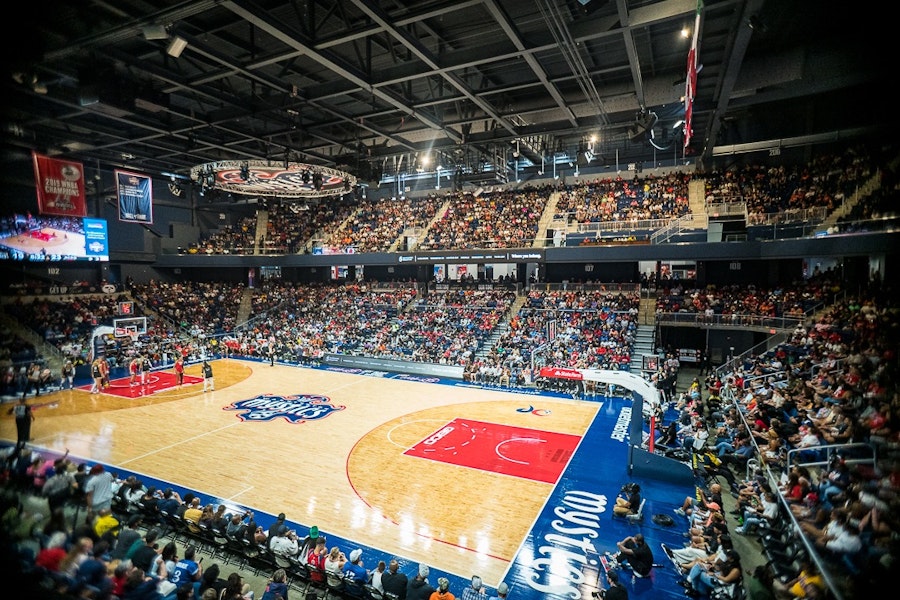 A lively crowd fills the stands at a Washington Mystics basketball game, with players in action on the court at the Entertainment and Sports Arena.