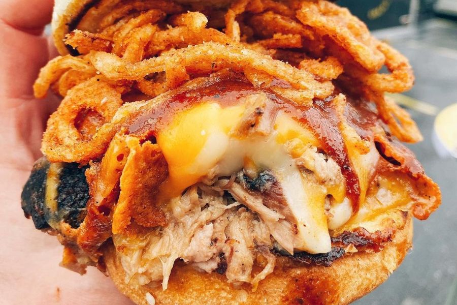 close-up of the Big Cheese Sandwich at Federalist Pig with layers of melted cheese, crispy onions and barbecue sauce on top of pulled pork