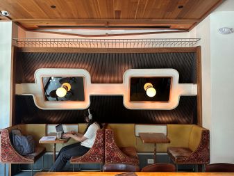 A person wearing headphones works at a booth in a stylish café with retro lighting and mid-century modern decor.