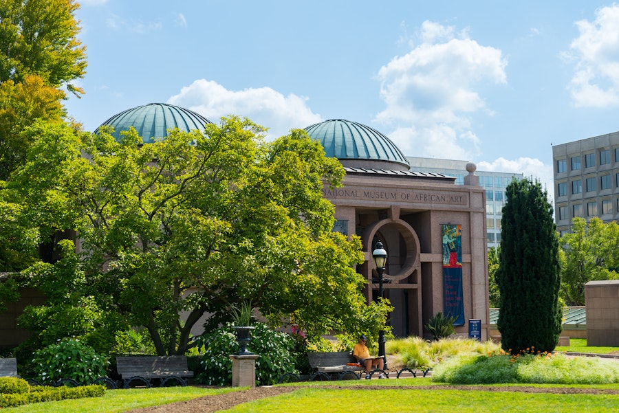 The National Museum of African Art is framed by lush trees and landscaped gardens on a sunny day.