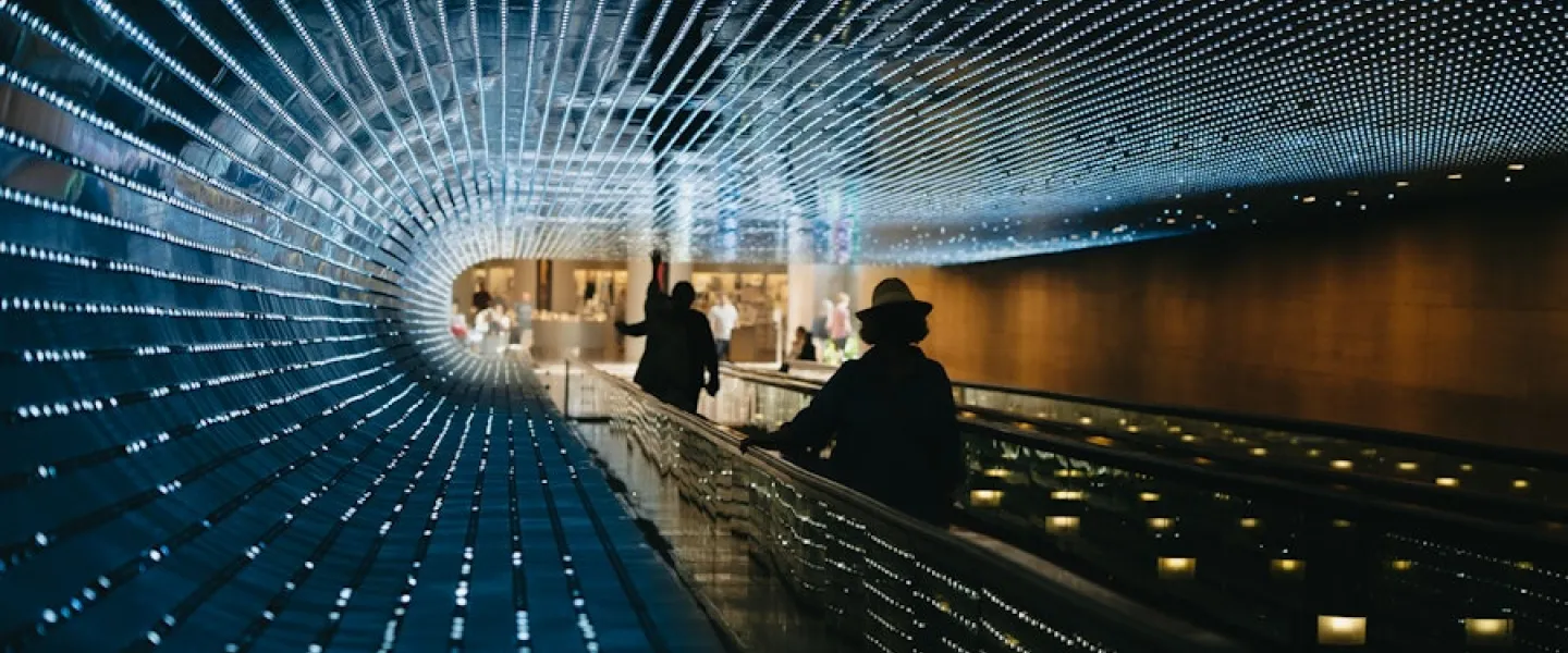 An illuminated walkway tunnel with a dynamic light display, creating an immersive and futuristic experience as visitors move through.