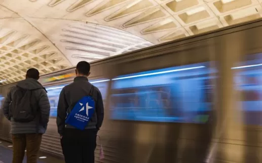 a student with an aef backpack stands as a dc metro train speeds by in the background
