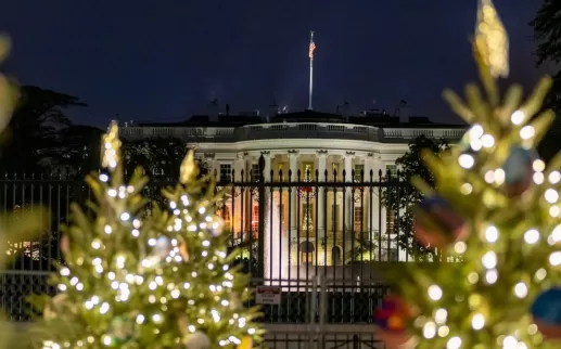 White House decorated for the holidays with Christmas trees in front and festive lights.
