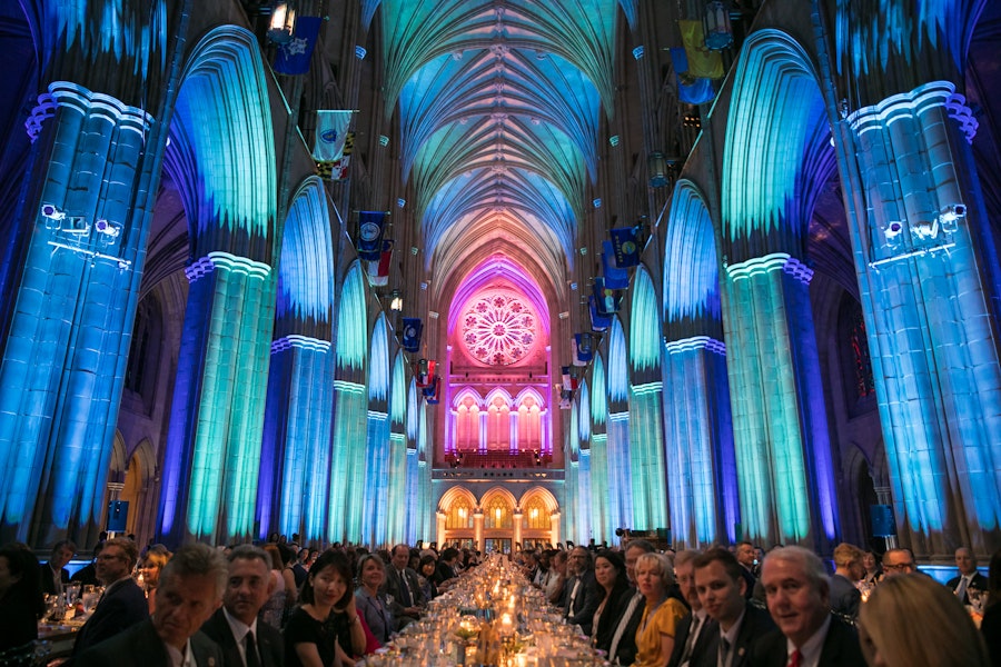 long banquet tables are full of event goers inside the Washington National Cathedral, with tall arches and dramatic, colorful lighting