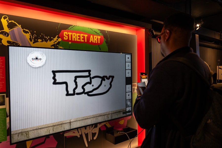 A visitor engages with a digital street art experience, drawing graffiti-style designs on an interactive screen.