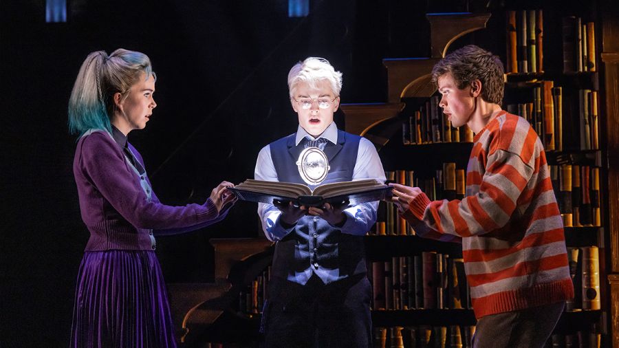 Three characters intensely examine a glowing magical object in a dramatic scene from Harry Potter and the Cursed Child.