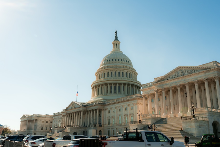 Cars park along the street in front of the U.S. Capitol as warm late-afternoon sunlight illuminates the dome and columns.