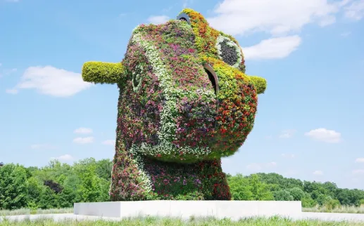 Jeff Koons’s “Split-Rocker” is a massive floral sculpture shaped like a rocking horse head, covered in colorful blooming plants.
