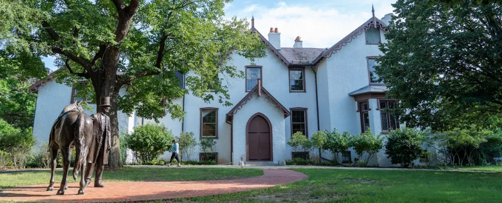 A statue of Abraham Lincoln with his horse stands before the historic Lincoln’s Cottage, surrounded by trees and greenery.